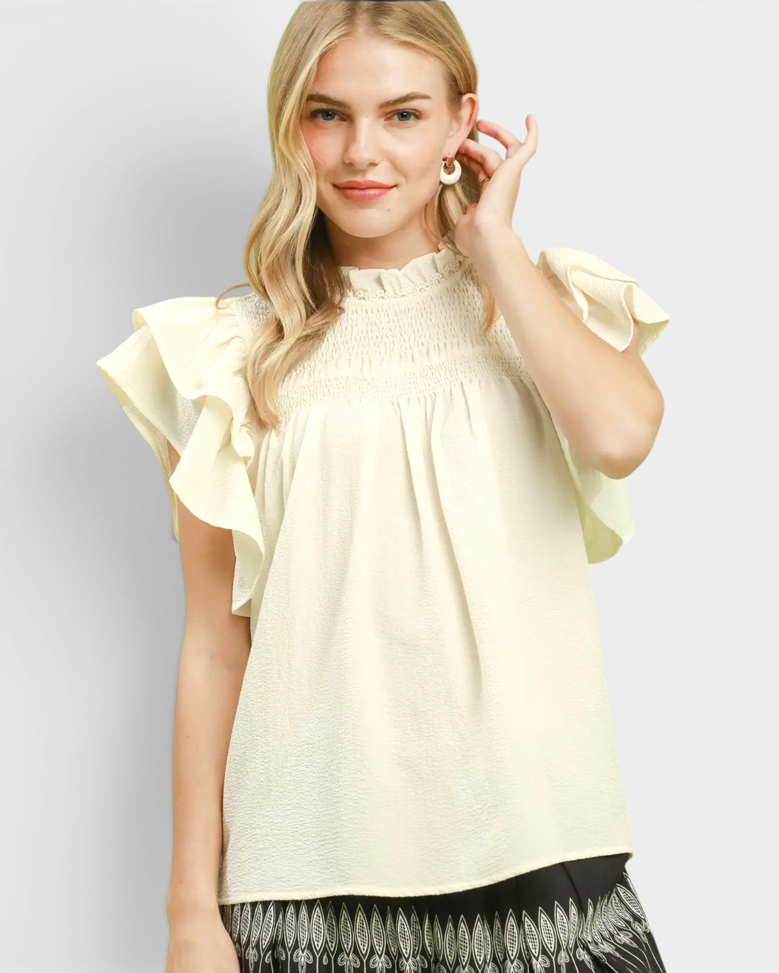Woman wearing a light yellow blouse with ruffled sleeves on a plain background