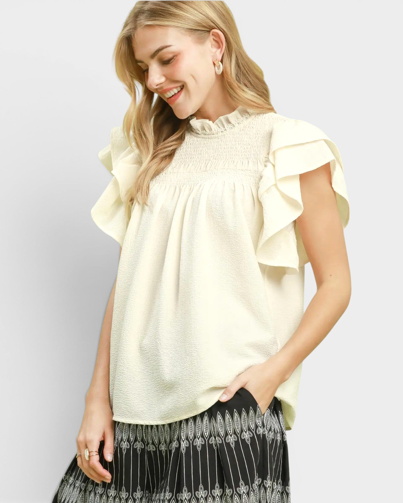 Woman wearing a light-colored blouse with ruffled sleeves on a plain background