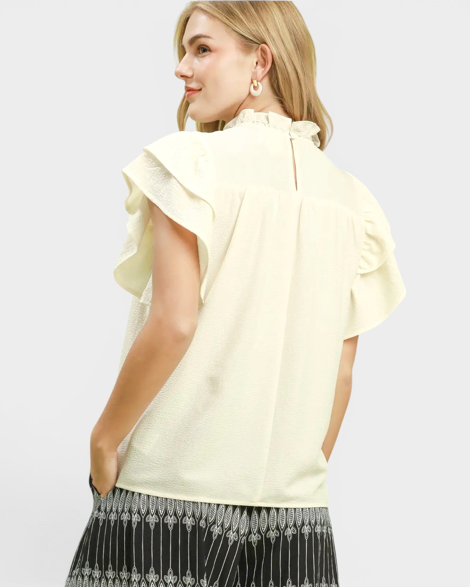 Woman wearing a light yellow blouse with ruffled sleeves on a white background