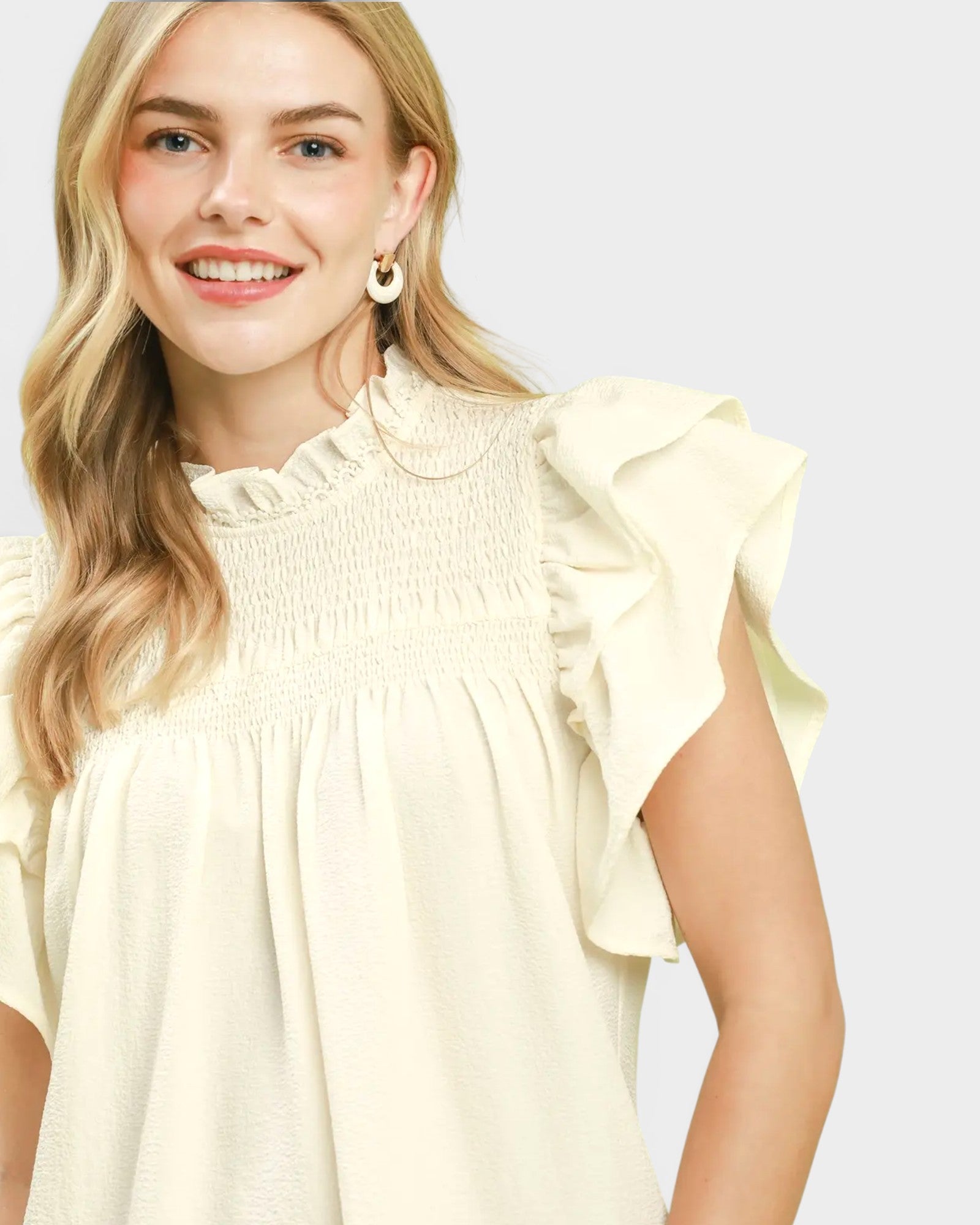 Woman wearing a light yellow blouse with ruffled sleeves on a plain background