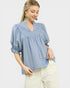 Woman wearing a blue blouse with ruffled details on a light gray background