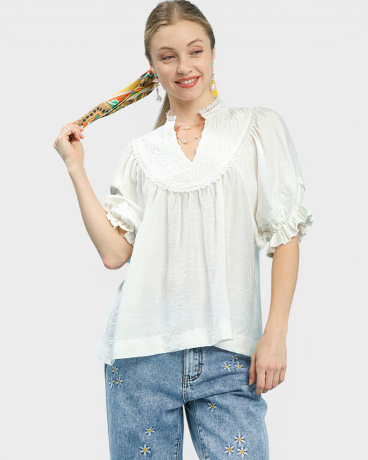 Woman wearing a white blouse and blue jeans with floral embroidery, holding a colorful bag.