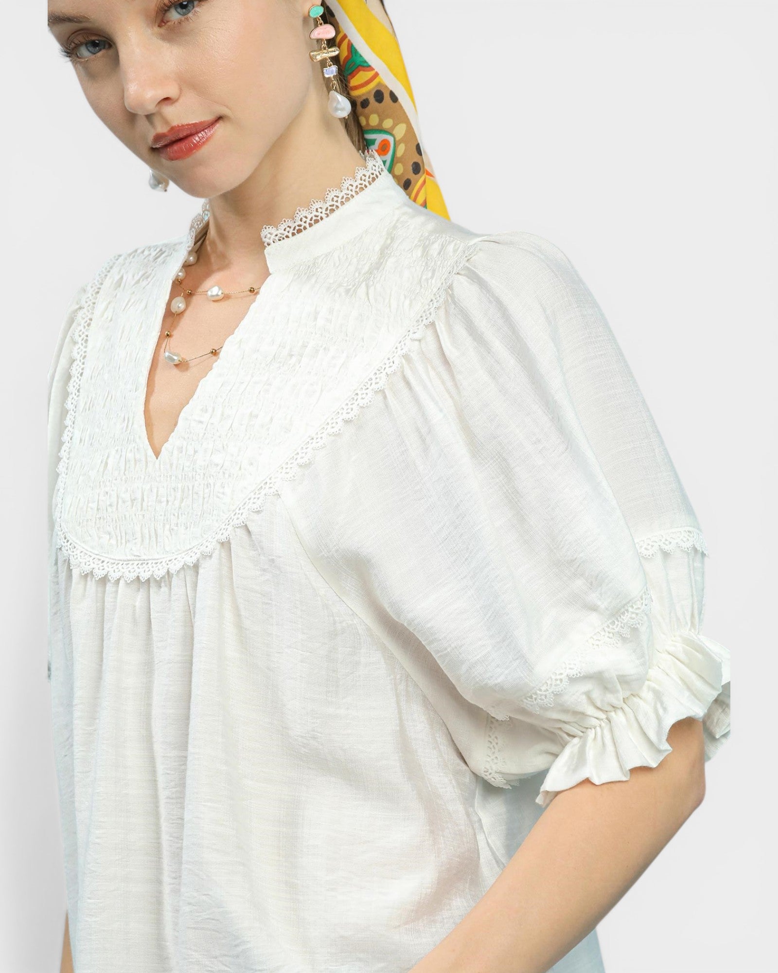 Woman wearing a white blouse with ruffled details on a plain background
