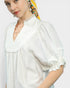 Woman wearing a white blouse with ruffled details on a plain background