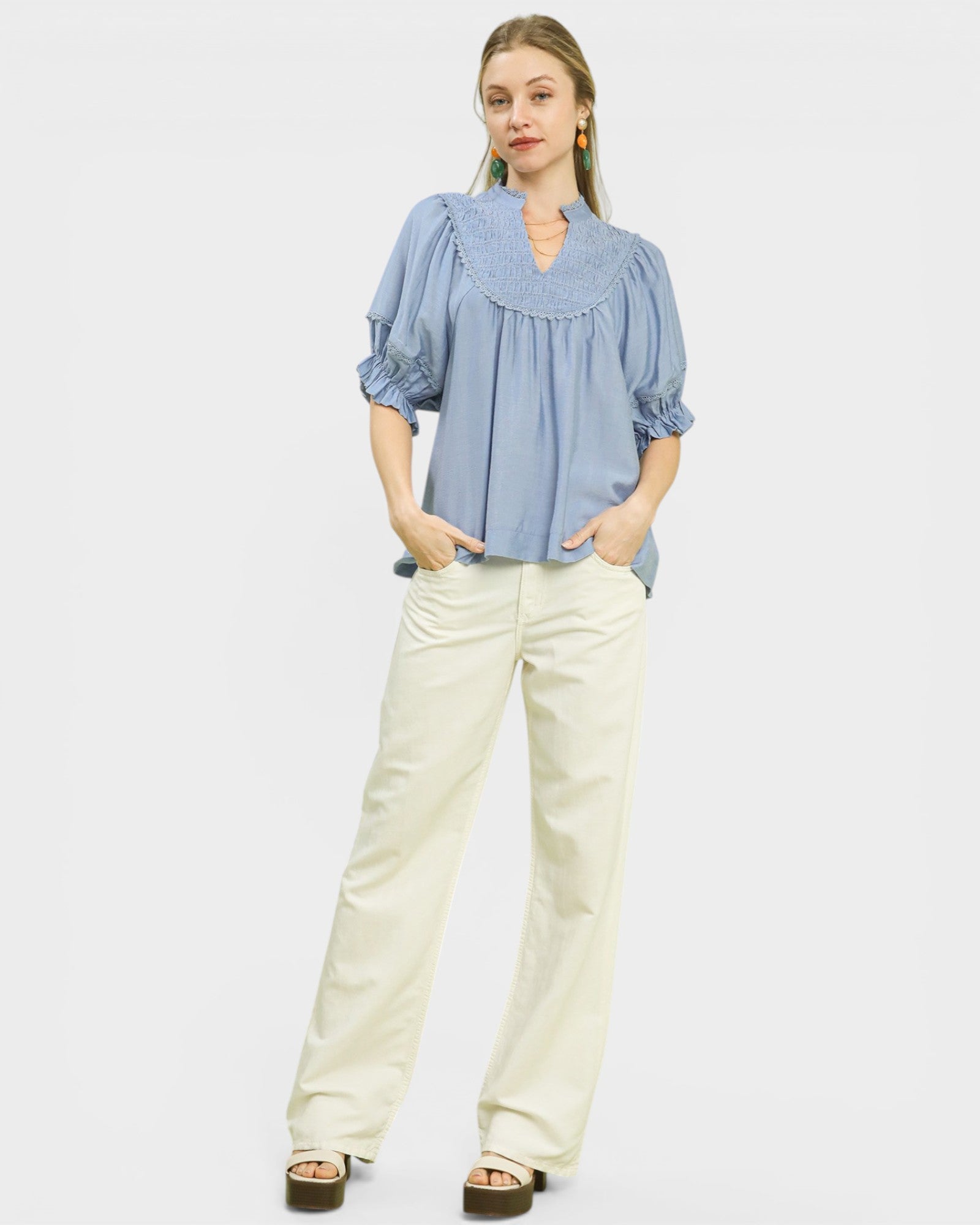 Woman wearing a blue blouse and white pants on a light gray background