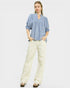 Woman wearing a blue blouse and white pants on a light gray background