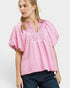 Woman wearing a pink and white checkered blouse with puffed sleeves on a plain background