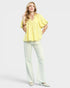 Woman wearing a yellow blouse and light green pants on a white background