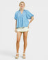 Woman wearing a blue checkered blouse and white shorts on a light gray background