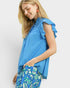 Woman wearing a blue top with ruffled sleeves and floral pants on a white background