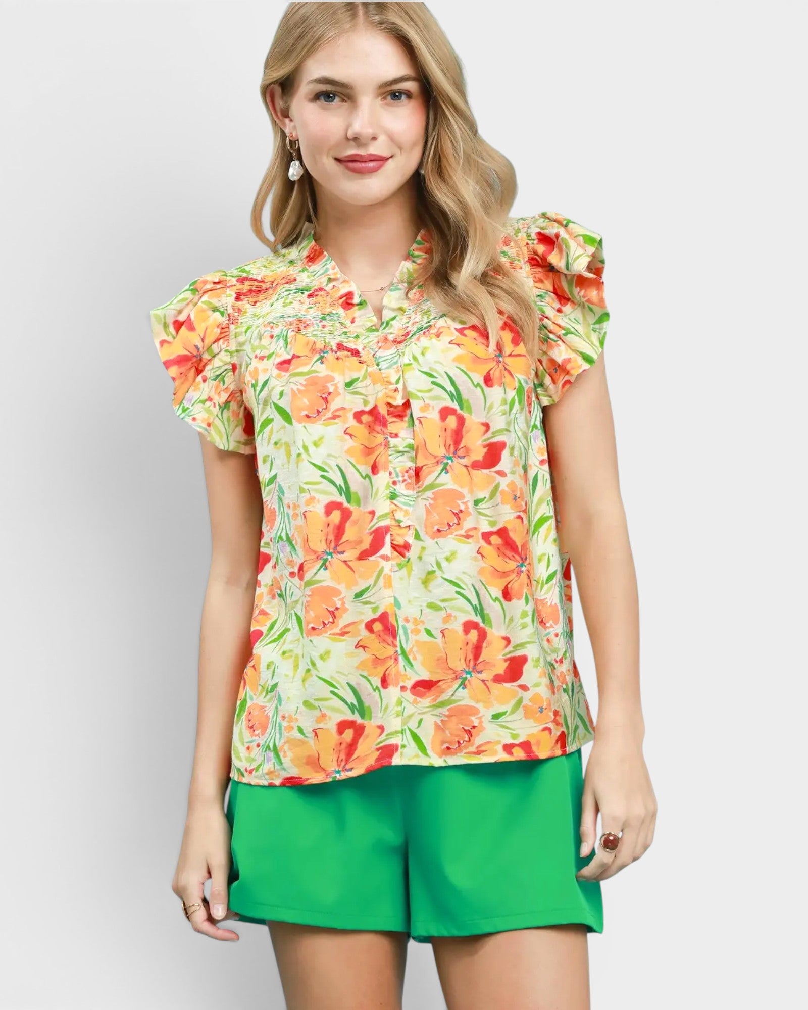 Woman wearing a colorful floral blouse and green shorts on a light gray background