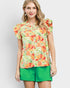 Woman wearing a colorful floral blouse and green shorts on a light gray background
