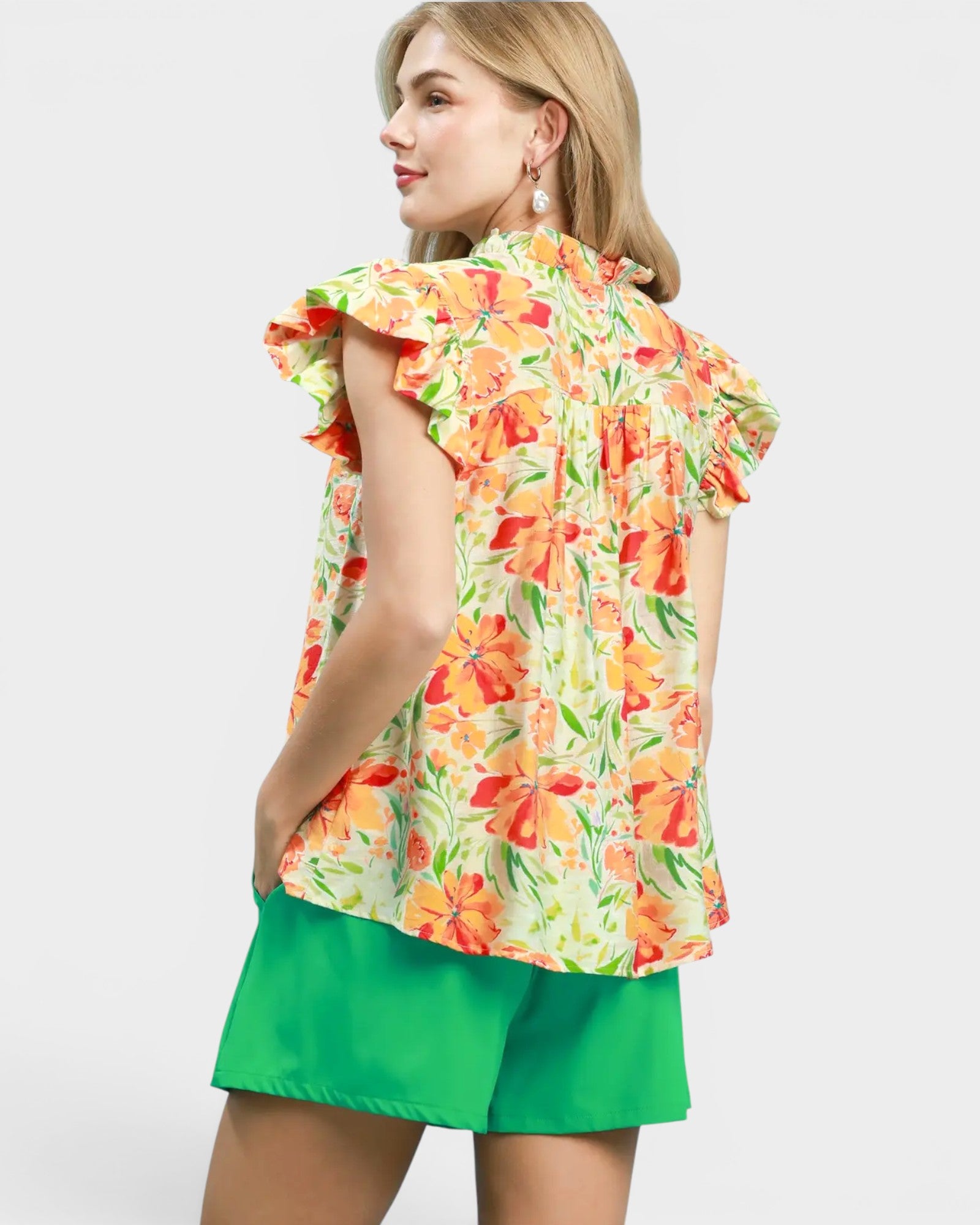 Woman wearing a colorful floral top and green shorts on a white background