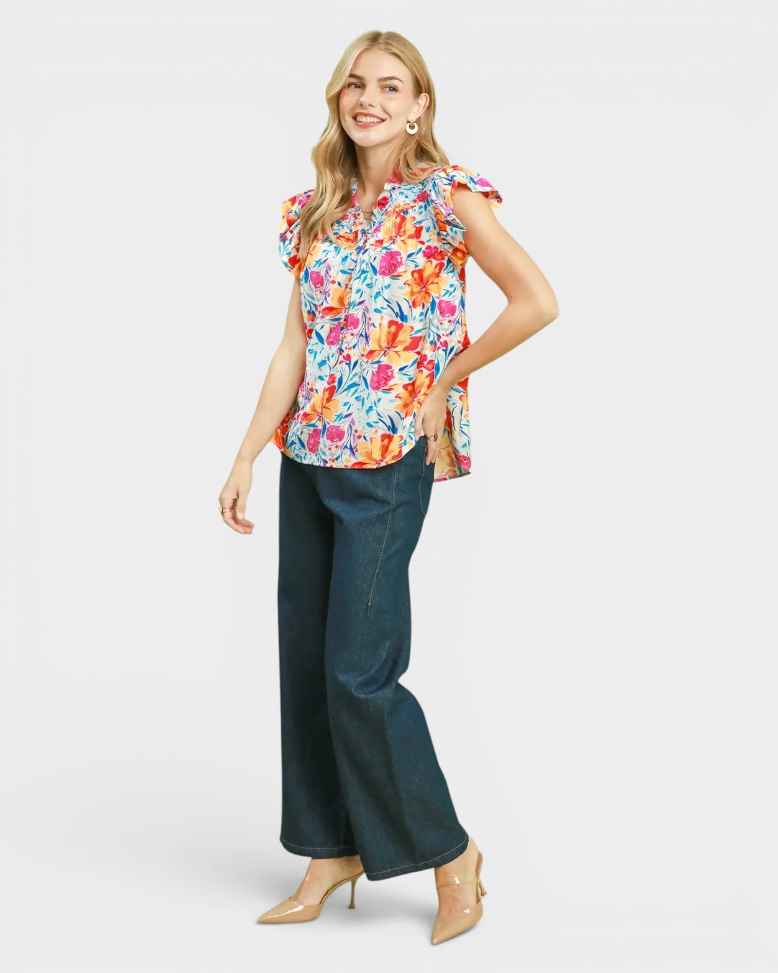 Woman wearing a colorful floral top and dark jeans on a white background