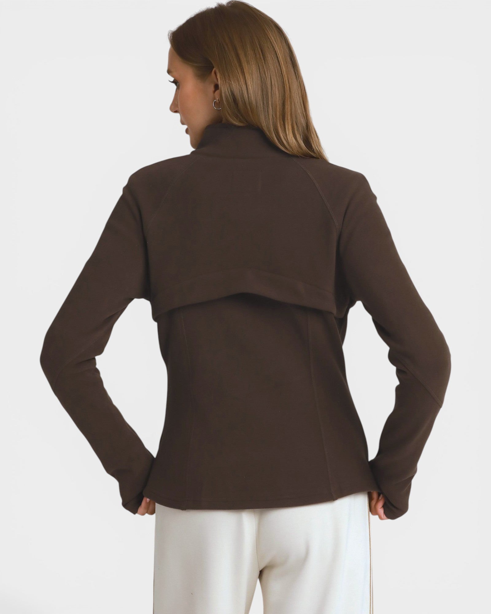 A woman shown from the back wearing a dark brown long-sleeve cropped jacket with a draped shoulder detail and white pants, against a light gray studio background.