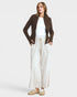 A woman modeling a dark brown knit zip-up cardigan over a white top and cream wide-leg trousers, paired with beige sneakers, against a light gray studio background.