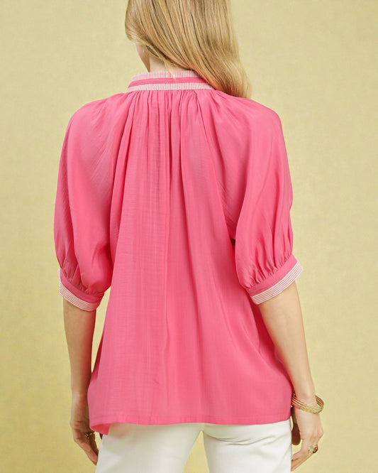 Person wearing a pink blouse with white trim on a beige background