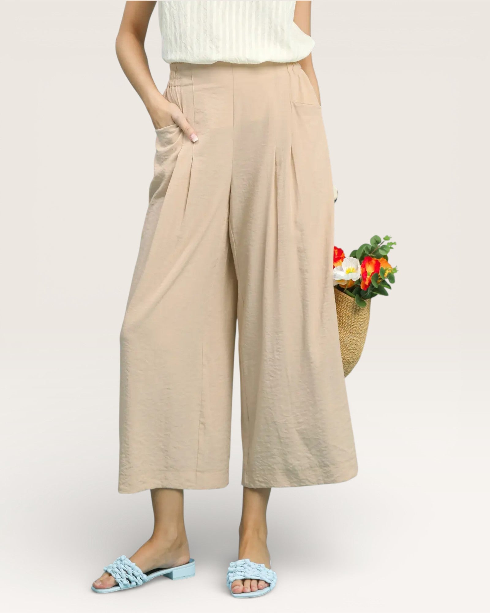 Person wearing beige wide-leg pants holding a basket of vegetables on a white background