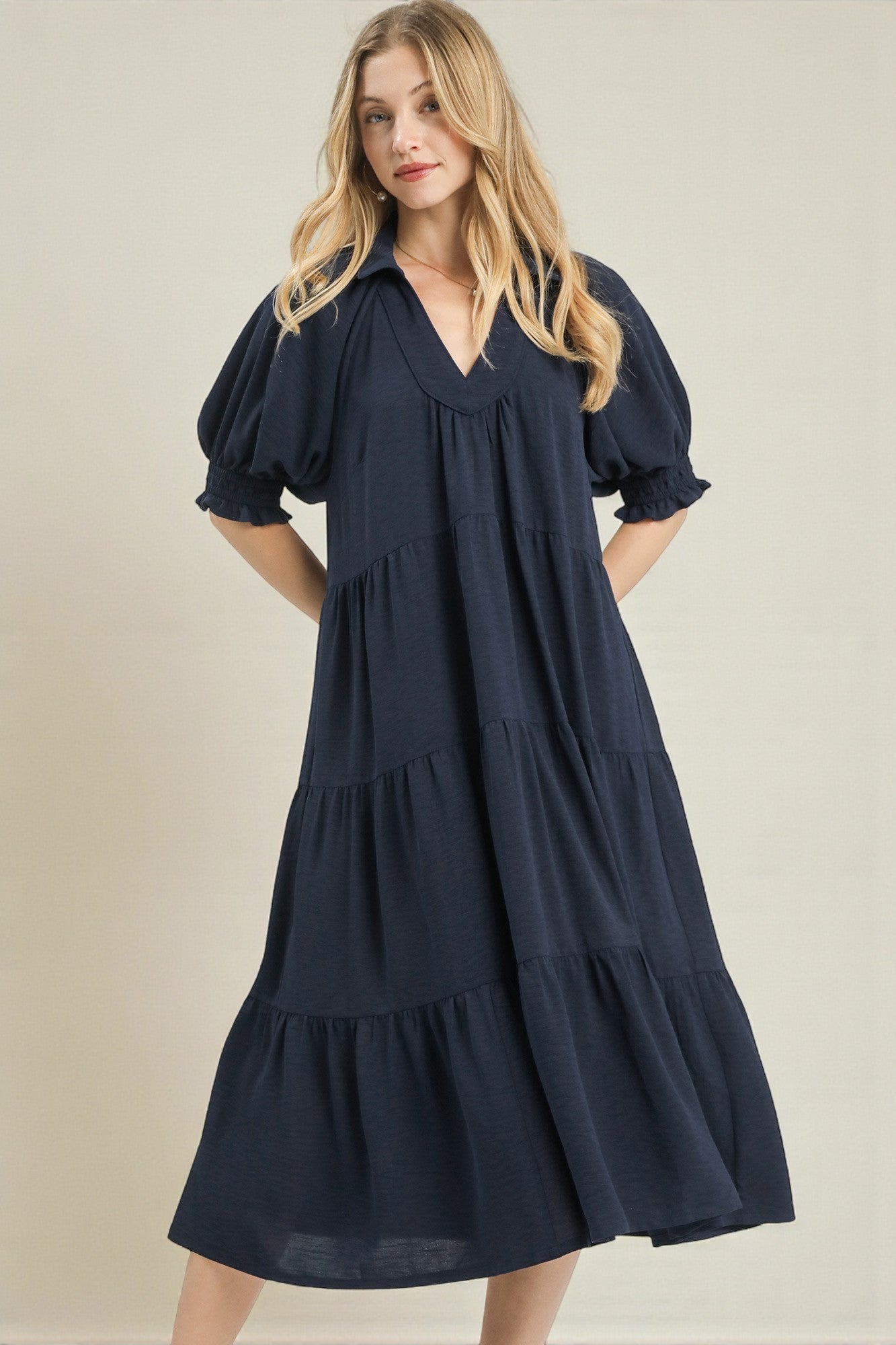 Woman wearing a navy blue dress with tiered layers on a beige background