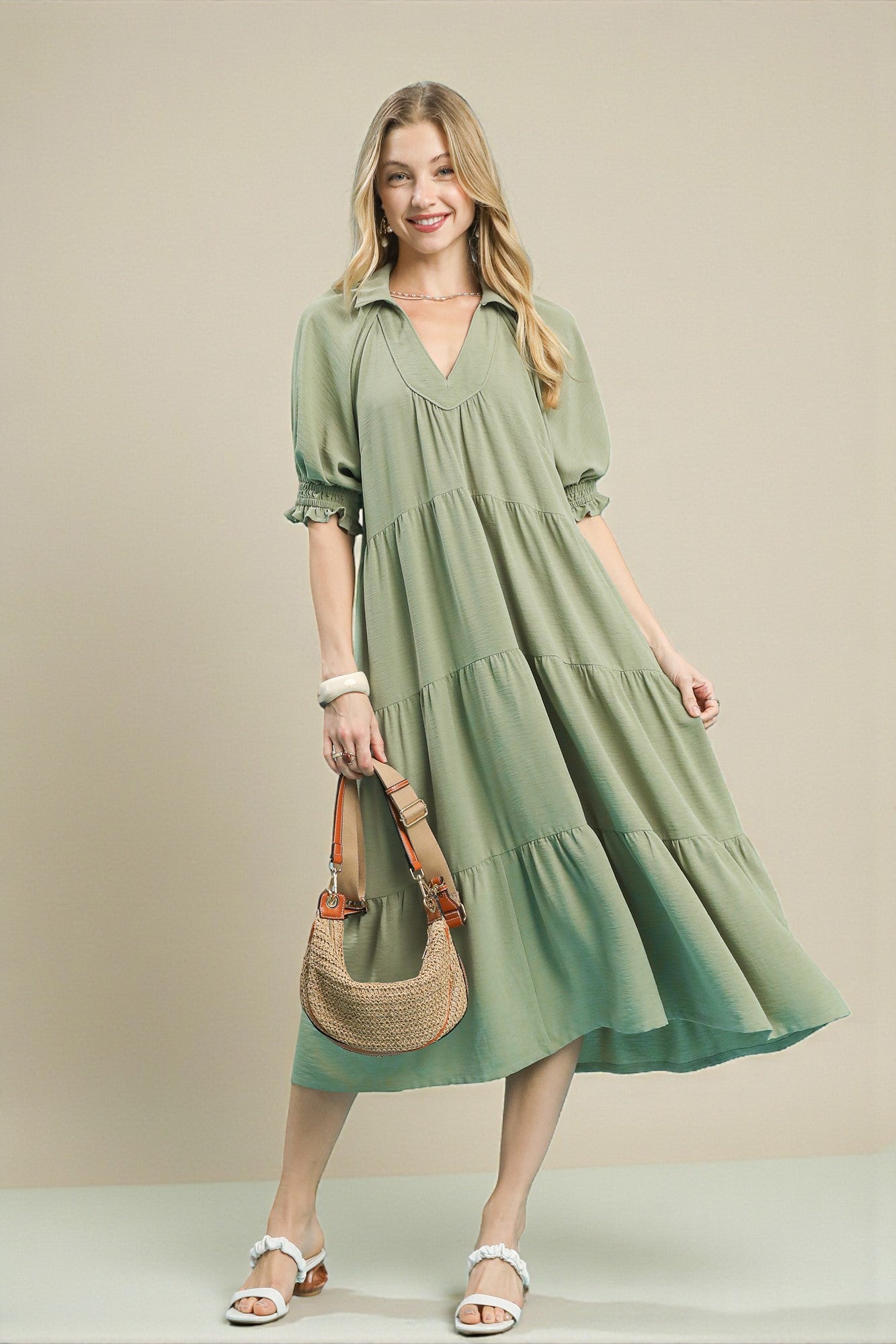Woman wearing a green dress holding a straw bag against a beige background