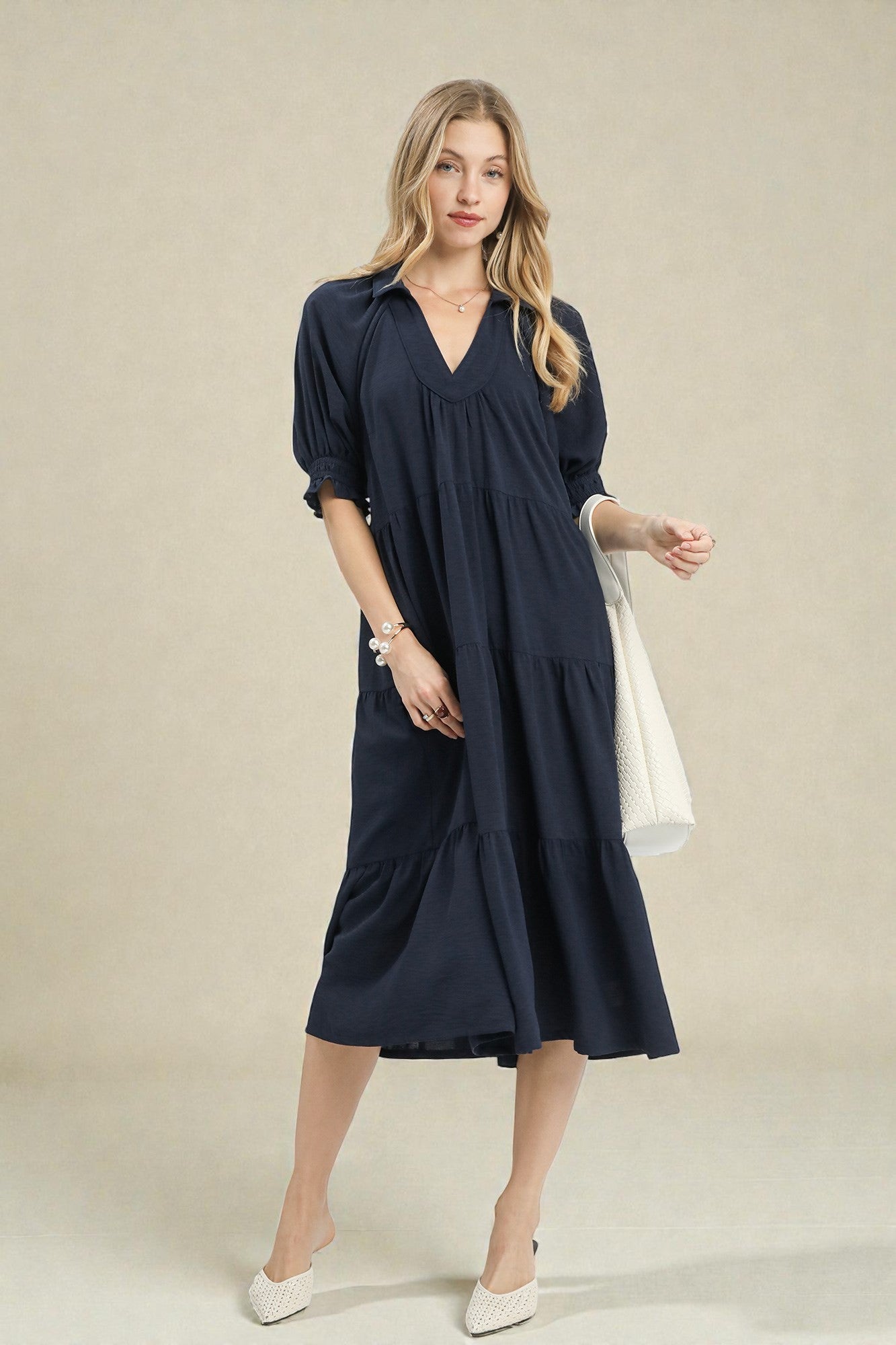 Woman wearing a navy blue dress holding a white bag on a beige background
