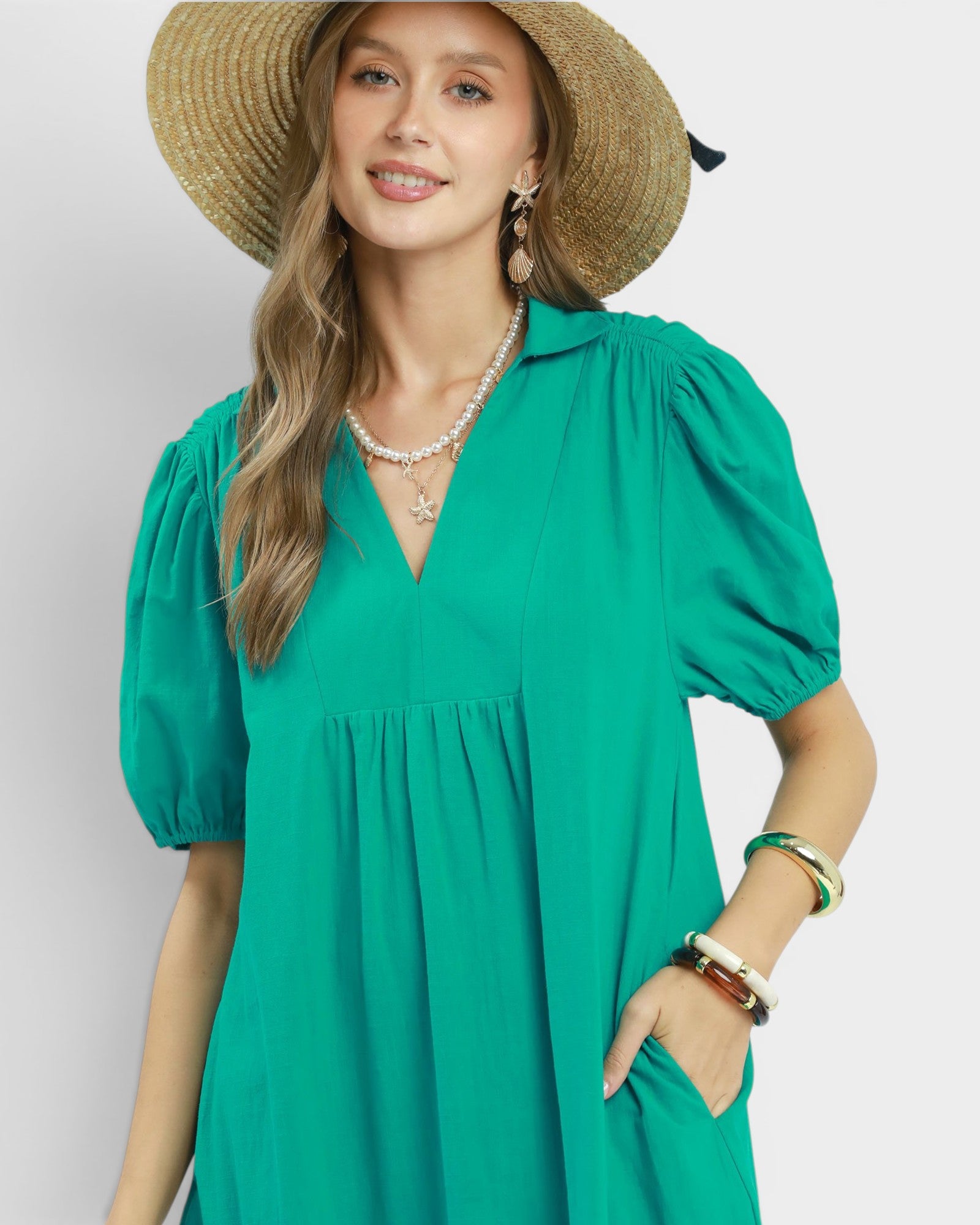 Woman wearing a green dress and straw hat on a plain background