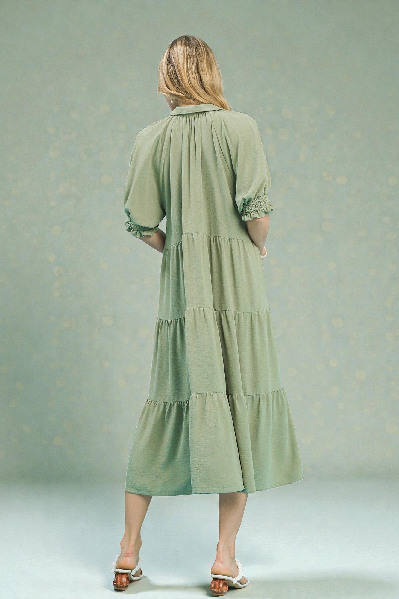 Woman wearing a green dress with tiered skirt against a light gray background