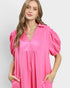 Woman wearing a bright pink dress with puff sleeves on a plain background
