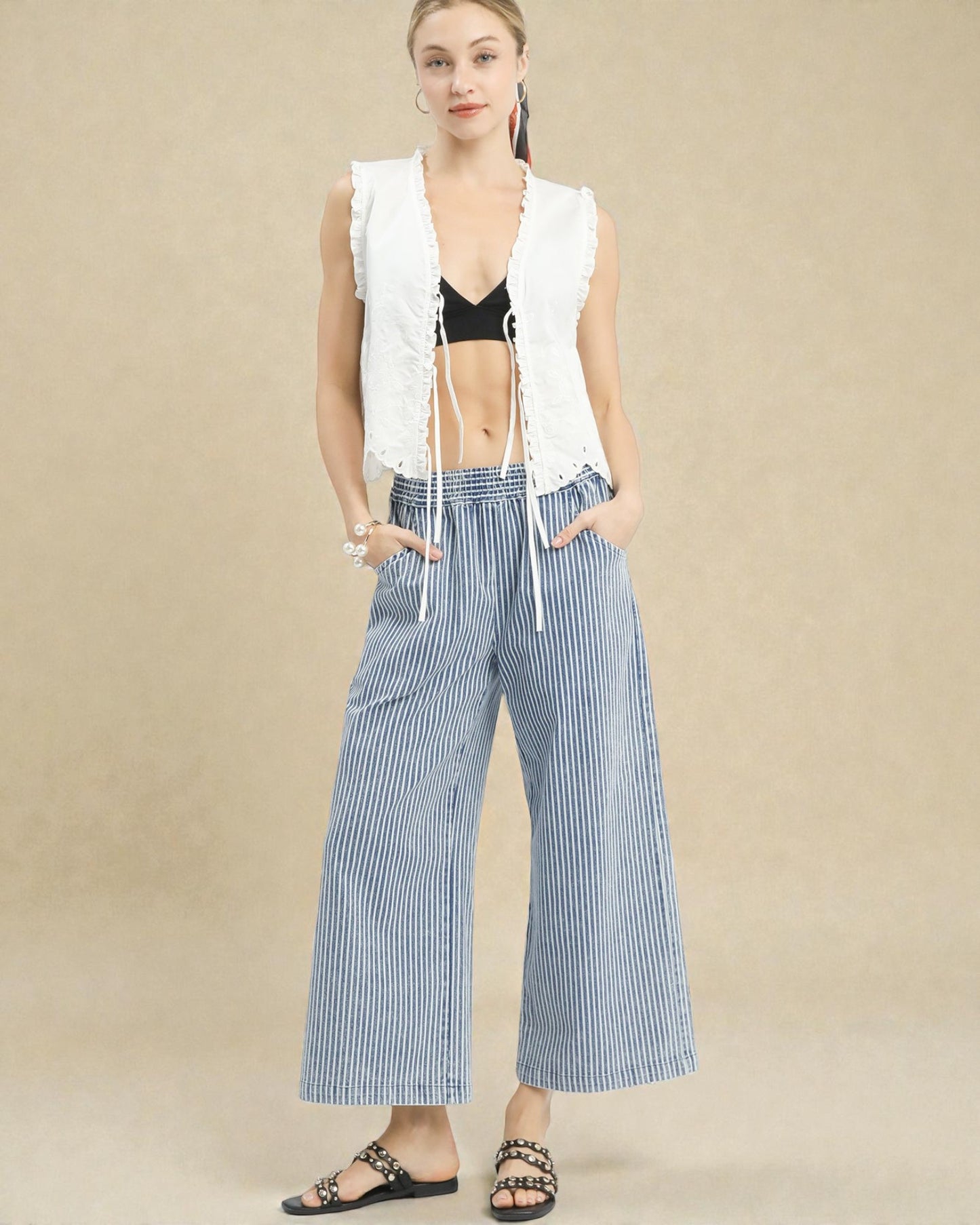 Woman wearing a white sleeveless top and blue striped pants on a beige background