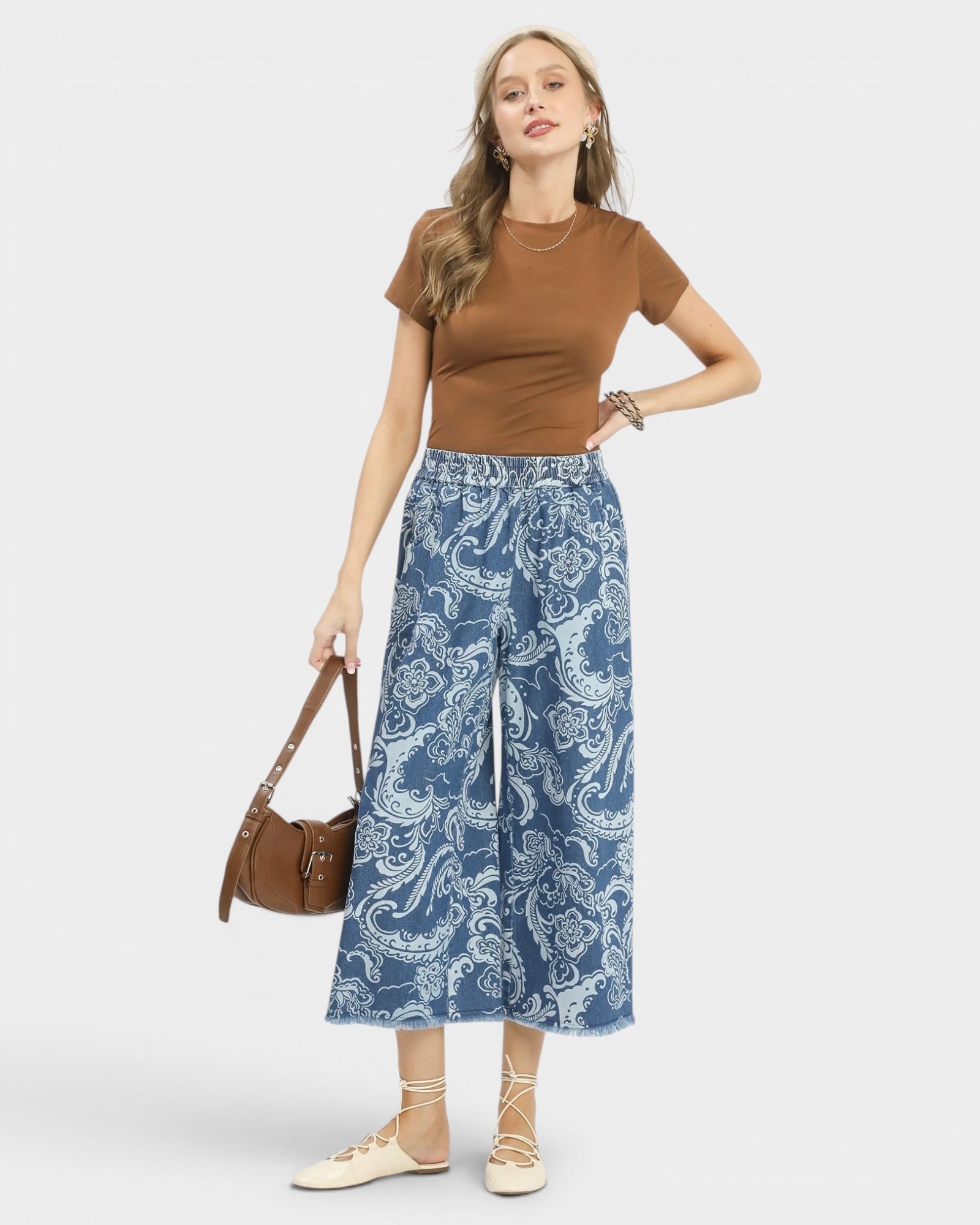 Woman wearing a brown top and blue patterned pants with a handbag on a white background