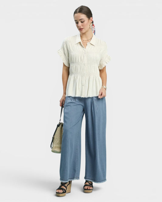 Woman wearing a white blouse and blue pants holding a straw bag on a white background