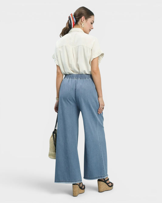 Woman wearing a white blouse and blue wide-leg pants on a white background