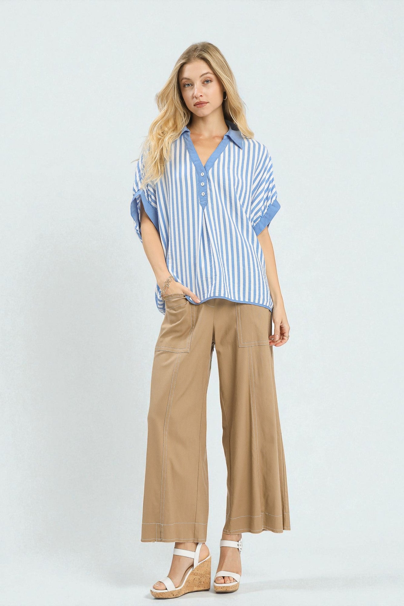 Woman wearing a blue striped shirt and beige pants on a white background