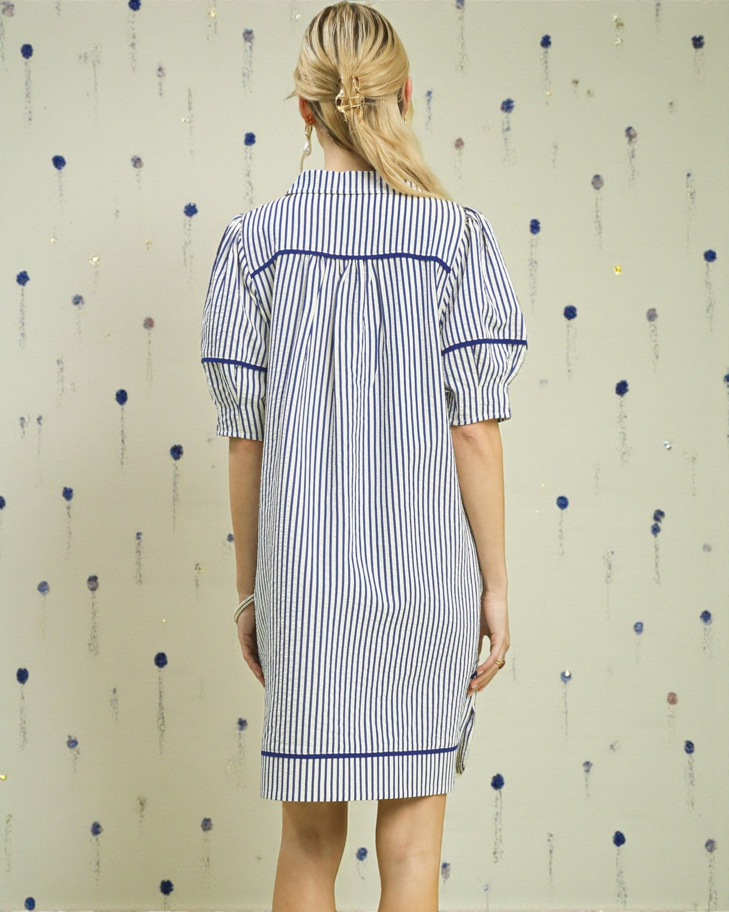 Woman wearing a blue and white striped dress against a patterned wall.
