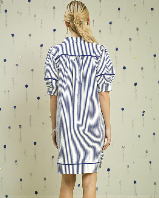 Woman wearing a blue and white striped dress against a patterned wall.