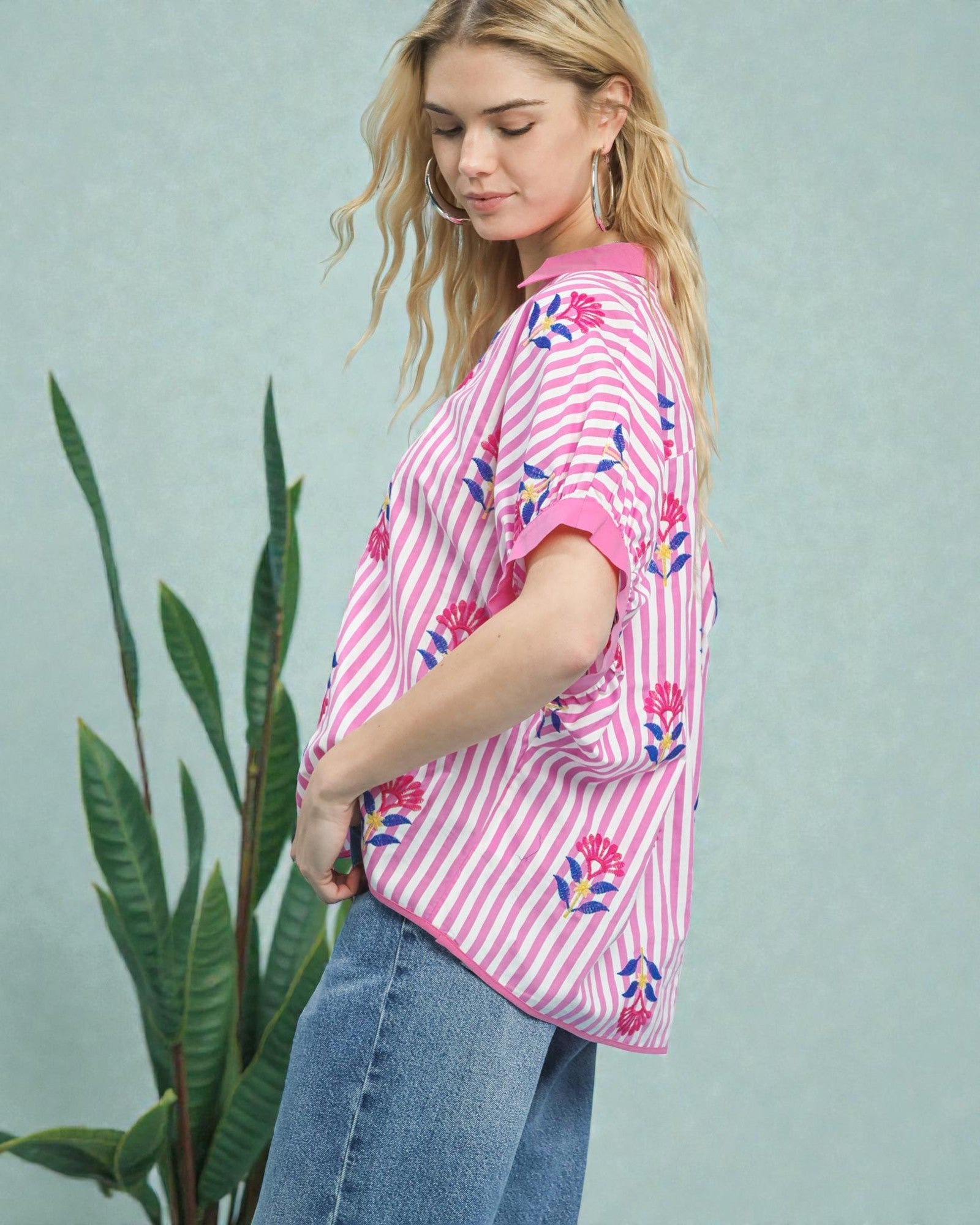 Woman wearing a pink and white striped shirt with floral patterns, standing against a light green background.