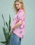 Woman wearing a pink and white striped shirt with floral patterns, standing against a light green background.