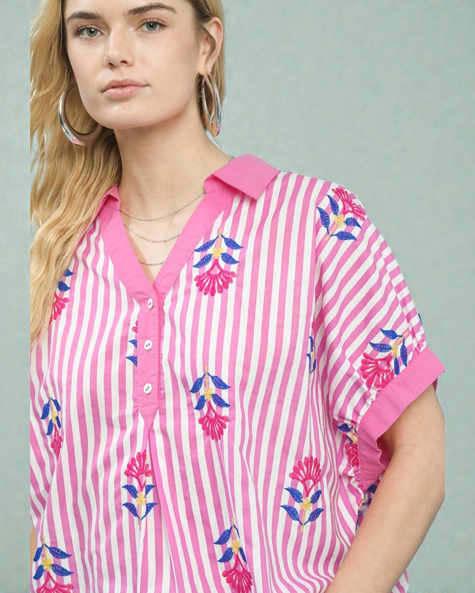 Woman wearing a pink and white striped shirt with floral patterns on a gray background