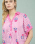 Woman wearing a pink and white striped shirt with floral patterns on a gray background