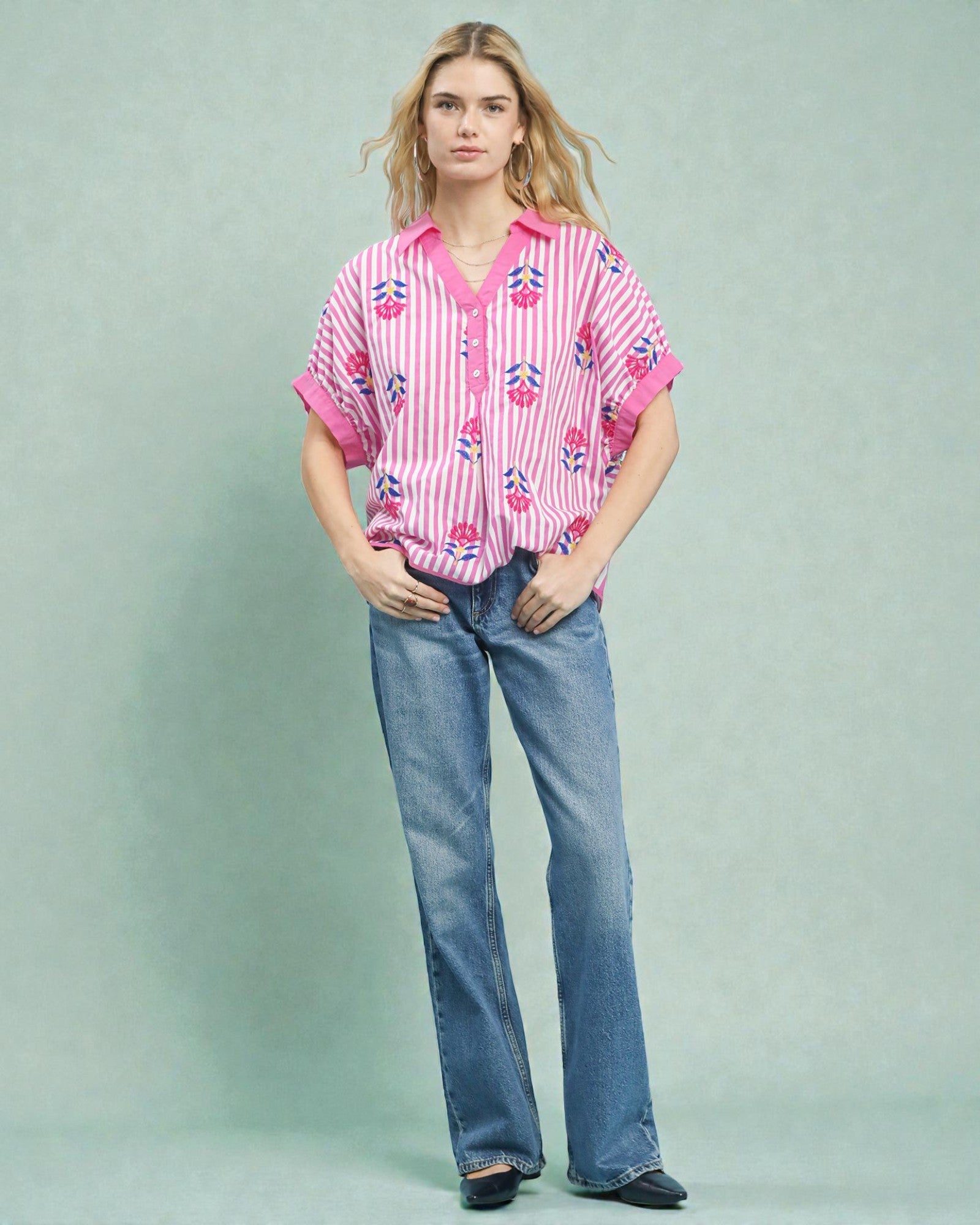 Woman wearing a pink floral blouse and blue jeans on a light gray background