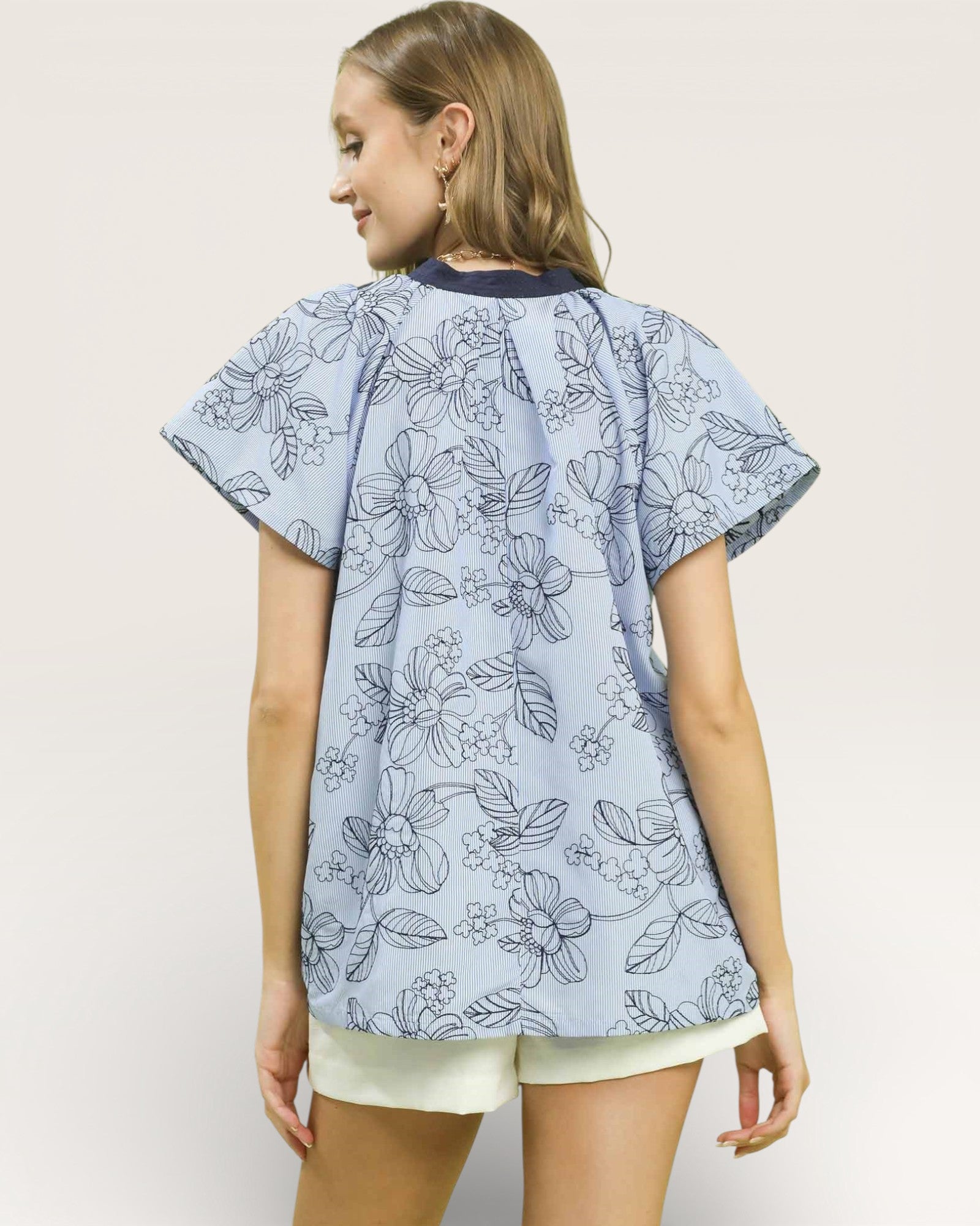 Woman wearing a light blue floral patterned top on a plain background