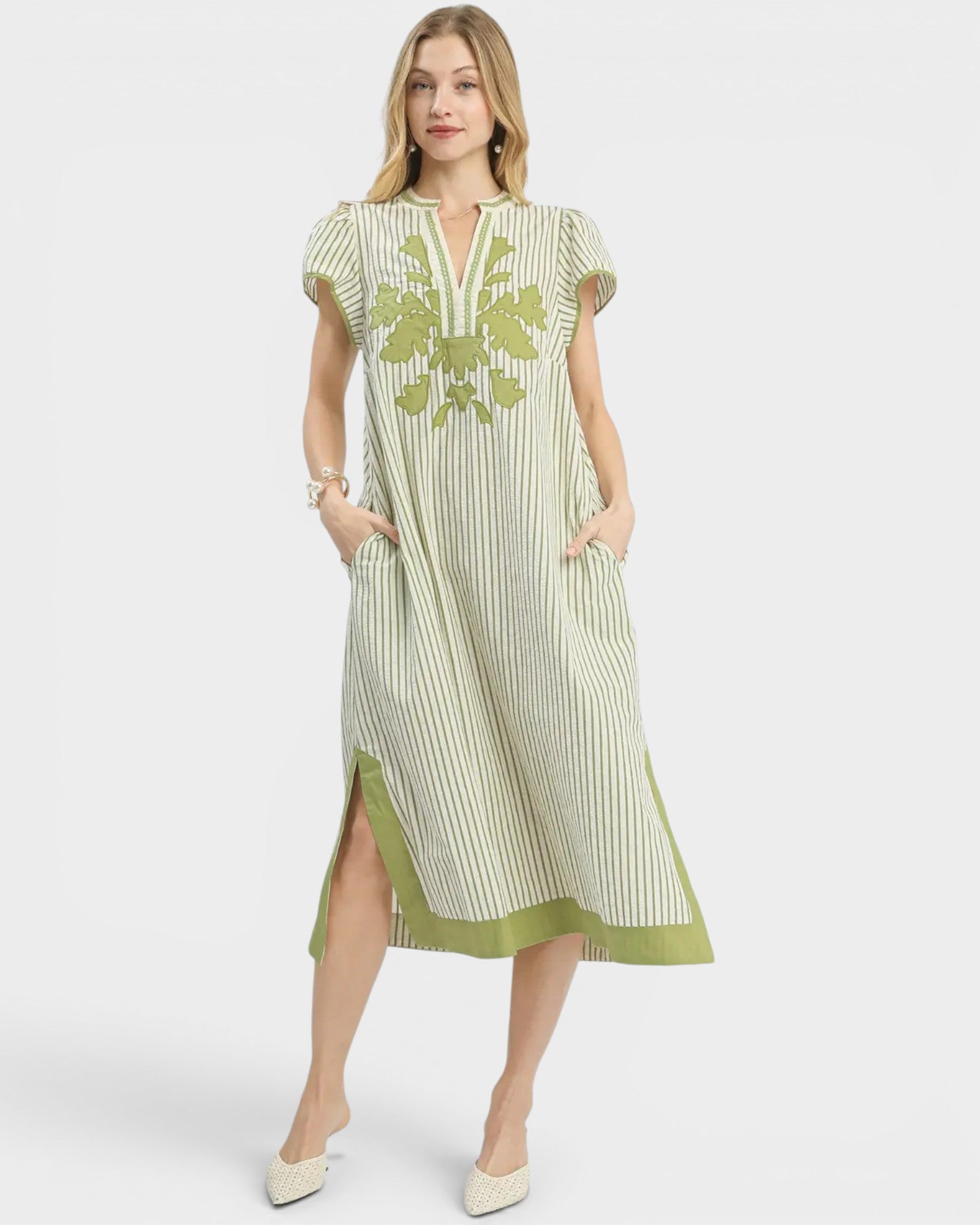 Woman wearing a green and white striped dress with floral embroidery on a white background