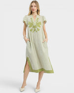 Woman wearing a green and white striped dress with floral embroidery on a white background