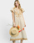 Woman wearing a beige dress with floral patterns, holding a straw hat and flowers on a white background