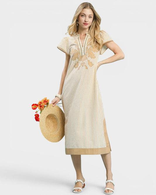 Woman wearing a beige dress with floral embroidery, holding a straw hat and flowers, on a white background