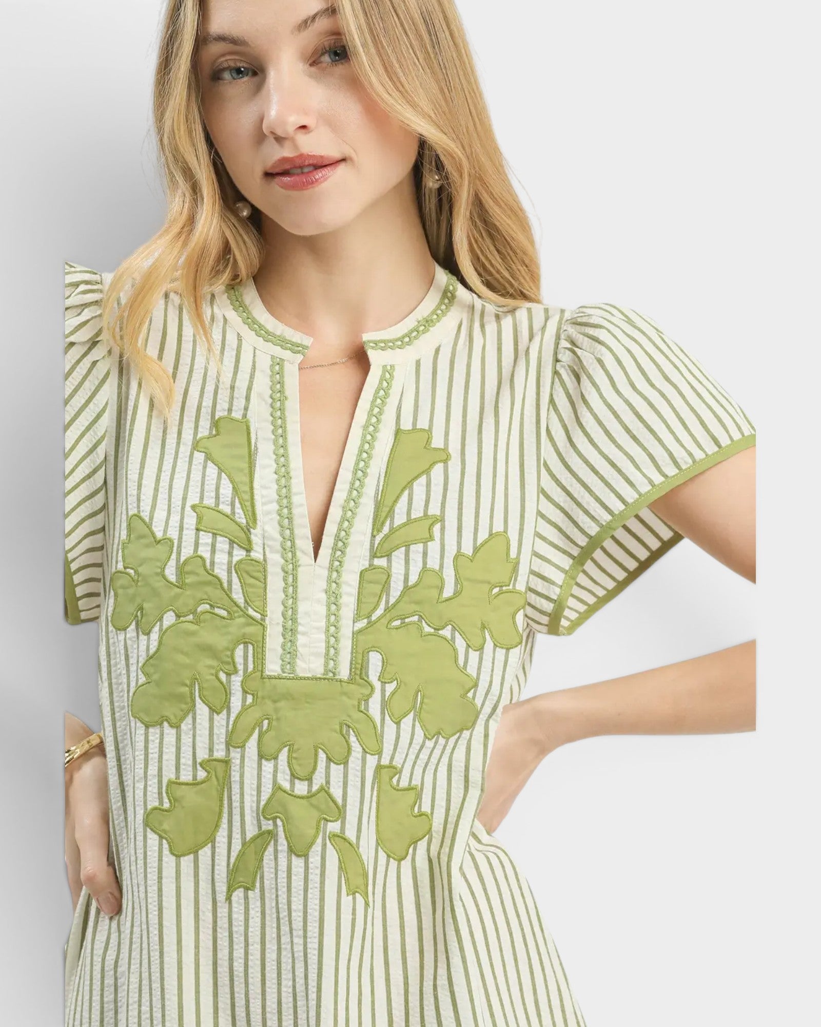 Woman wearing a green and white dress with floral embroidery on a light gray background