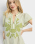 Woman wearing a green and white dress with floral embroidery on a light gray background
