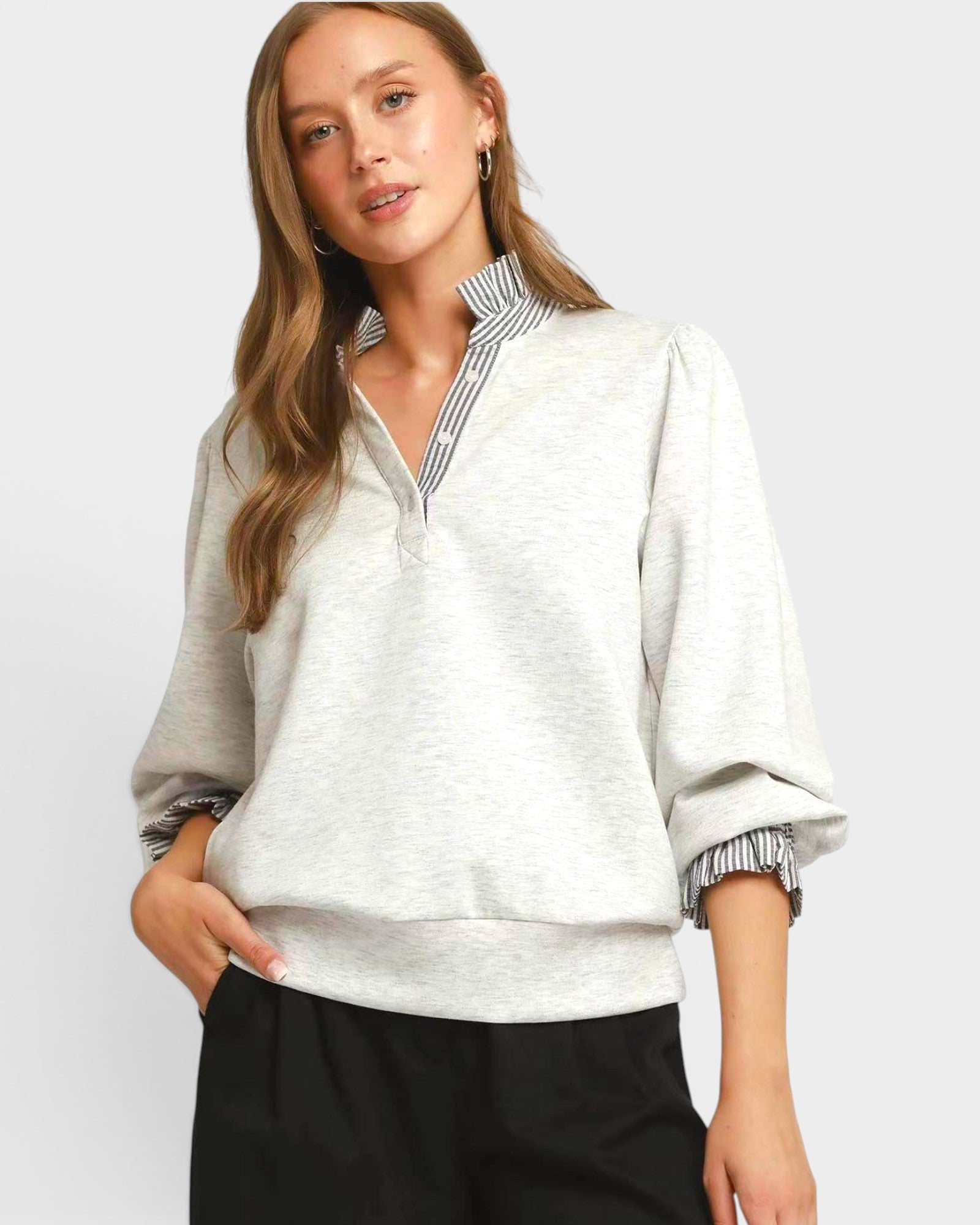 Woman wearing a light gray sweater with a striped collar against a white background