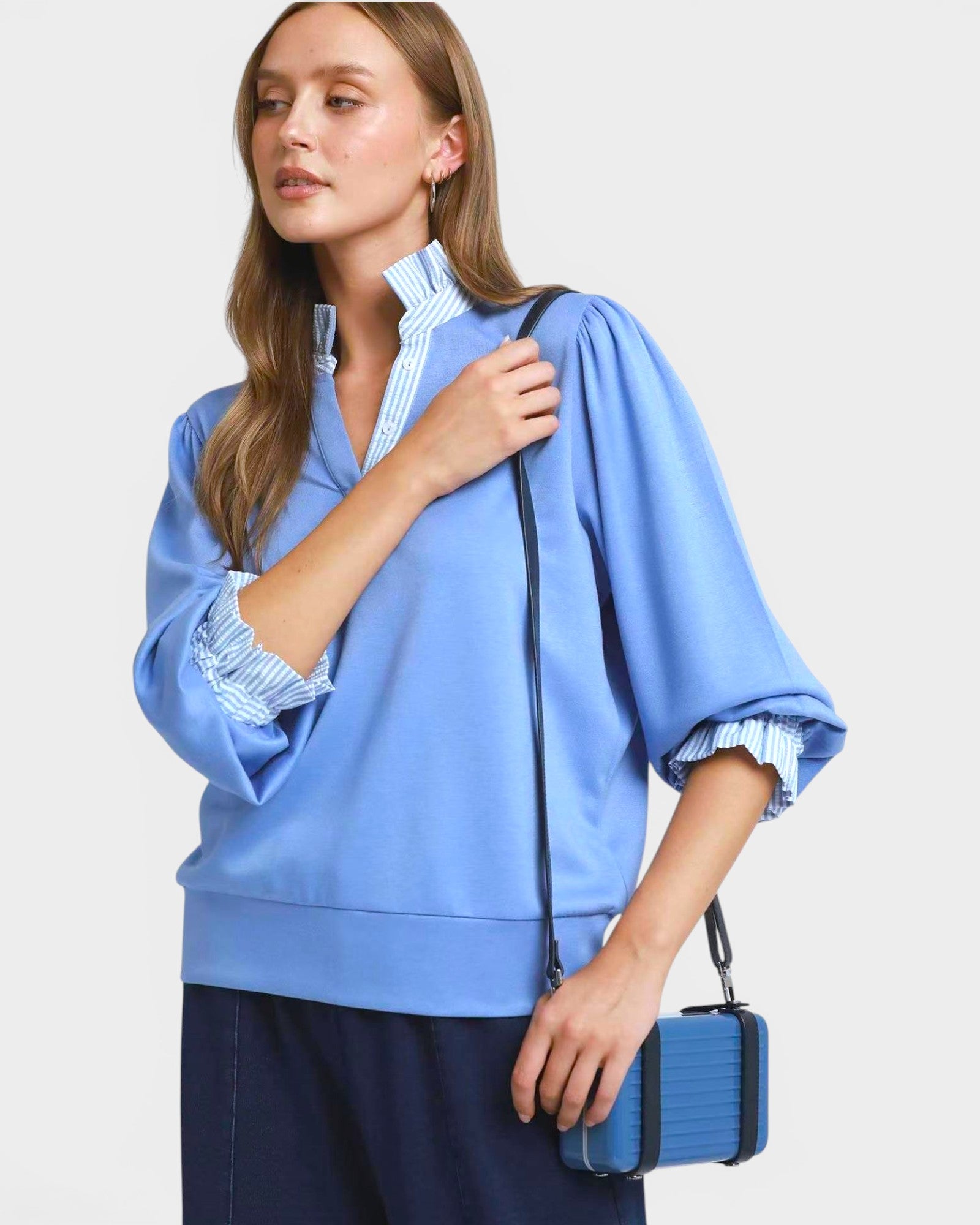 Woman wearing a blue blouse with rolled-up sleeves, holding a matching blue handbag against a light background.