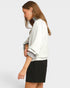 Woman wearing a white sweater over a striped shirt with a black skirt on a light gray background